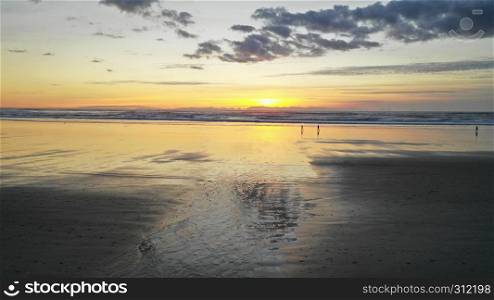People walk on the beach reflection late afternoon at dusk in Cannon Beach Oregon