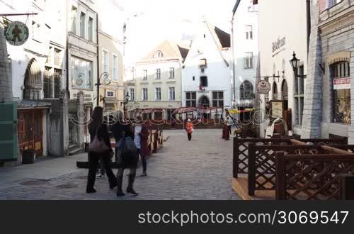 People walking along old narrow street with ancient buildings