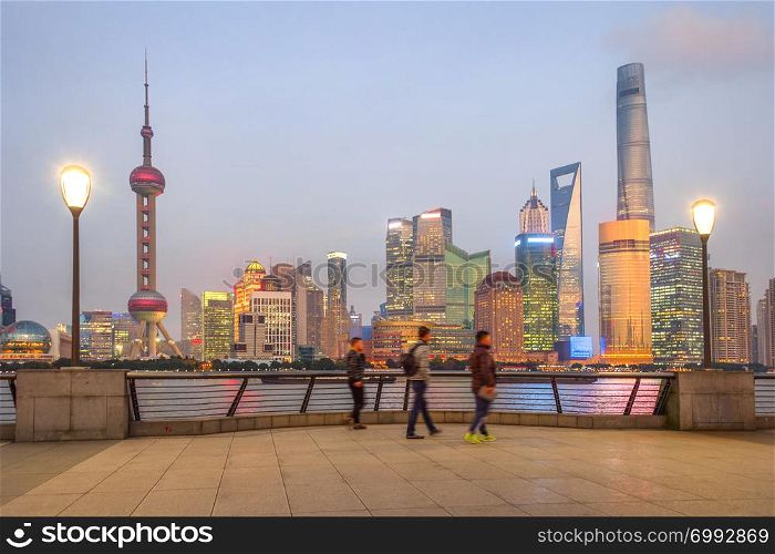 People walking at embankment enjoying illuminated evening Shanghai cityscape view, China