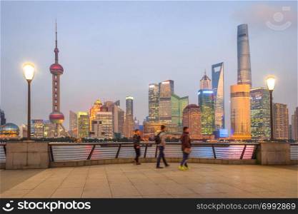 People walking at embankment enjoying illuminated evening Shanghai cityscape view, China