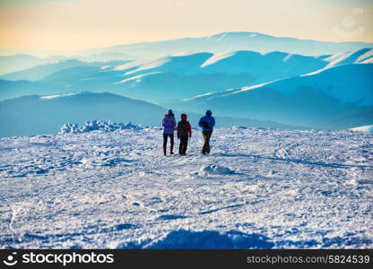 People walking at sunset in winter mountains covered with snow