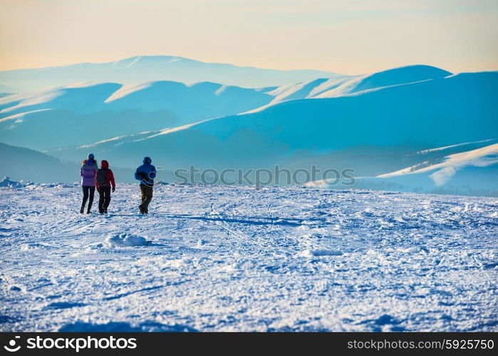 People walking at sunset in winter mountains covered with snow