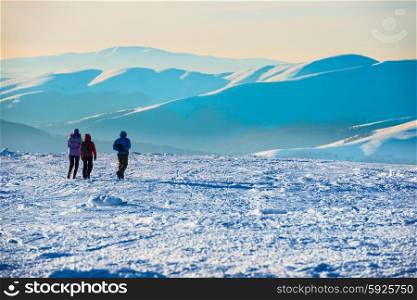 People walking at sunset in winter mountains covered with snow