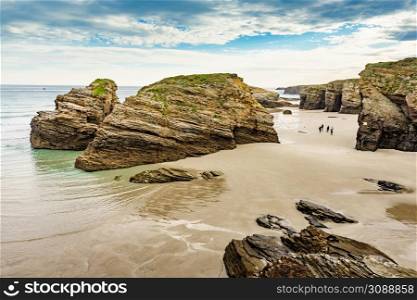 People walking on Cathedrals Beach at low tide, Playa las Catedrales in Ribadeo, province of Lugo, Galicia. Cantabric coast in northern Spain. Tourist place.. People walking on Beach Cathedrals Beach, Galicia Spain.