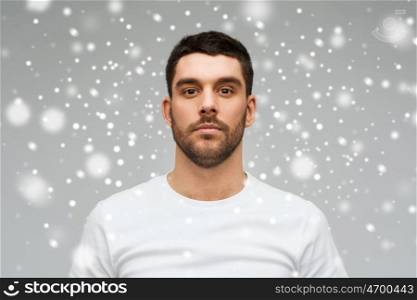people, winter and christmas concept - young man portrait over snow on gray background