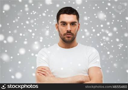 people, winter and christmas concept - young man with crossed arms over snow on gray background