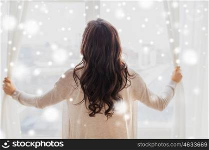 people, winter, christmas and hope concept - close up of happy woman opening window curtains at home over snow