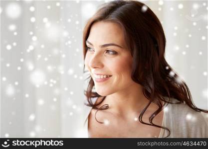 people, winter, christmas and leisure concept - close up of happy young woman looking through window at home over snow