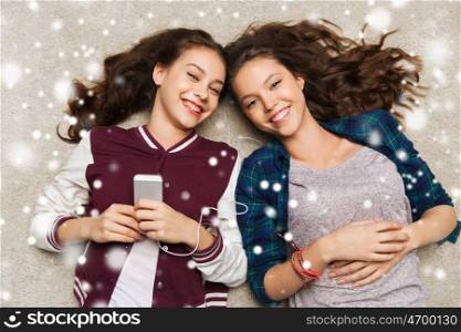 people, winter, christmas and technology concept - happy smiling pretty teenage girls or friends with smartphones and earphones listening to music over snow