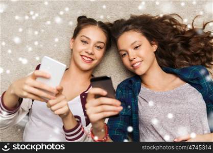 people, winter, christmas, technology and friendship concept - happy smiling pretty teenage girls or friends lying on floor with smartphones over snow