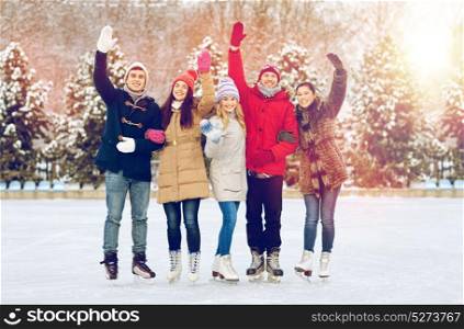 people, winter, friendship, sport and leisure concept - happy friends ice skating and waving hands on rink outdoors. happy friends ice skating on rink outdoors