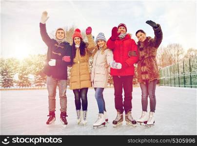 people, winter, friendship, sport and leisure concept - happy friends ice skating and waving hands on rink outdoors. happy friends ice skating on rink outdoors