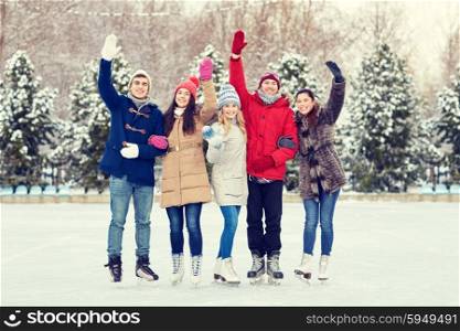 people, winter, friendship, sport and leisure concept - happy friends ice skating and waving hands on rink outdoors