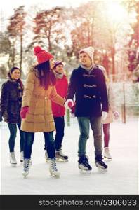 people, winter, friendship, sport and leisure concept - happy friends ice skating on rink outdoors. happy friends ice skating on rink outdoors