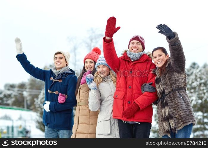 people, winter, friendship, sport and leisure concept - happy friends waving hands on ice rink outdoors
