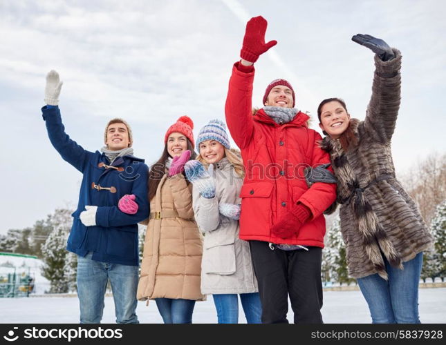 people, winter, friendship, sport and leisure concept - happy friends waving hands on ice rink outdoors