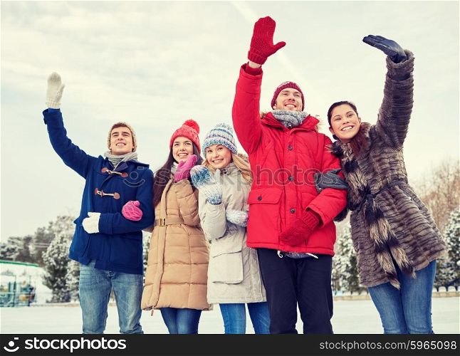people, winter, friendship, sport and leisure concept - happy friends waving hands on ice rink outdoors