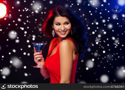 people, winter holidays, party, alcohol and leisure concept - beautiful sexy woman in red dress with cocktail glass at nightclub over snow