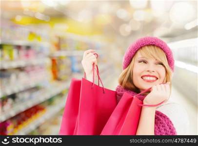 people, winter holidays, sale and consumerism concept - happy smiling woman in pink hat and scarf with many shopping bags over supermarket background