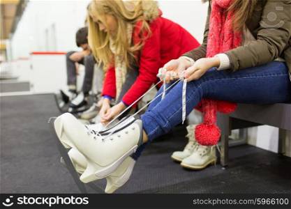 people, winter sport and leisure concept - close up of woman wearing and lacing skates on skating rink