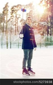 people, winter, technology and leisure concept - happy young man taking picture with smartphone selfie stick on ice skating rink outdoors. happy young man with smartphone on ice rink