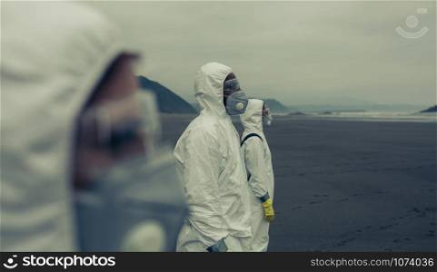 People with bacteriological protection suits on the beach looking at the sea. People with bacteriological protection suits looking at the sea