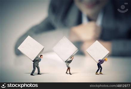 People with cubes. Businesswoman looking at miniature of people carrying white cube on back