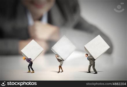 People with cubes. Businesswoman looking at miniature of people carrying white cube on back