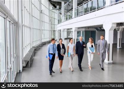 people, work and corporate concept - business team with folders walking along office building and talking. business people walking along office building