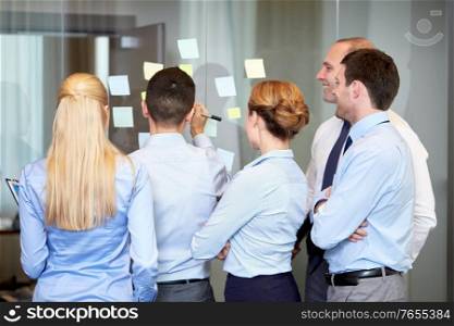 people, work and corporate concept - business team with sticky notes on glass wall at office. business team with sticky notes on glass at office