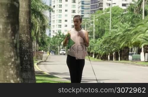 People working as dog-sitter, girl with french poodle dog in park. The young hispanic woman picks up her pet&acute;s poo with plastic bag