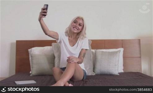People, young asian woman, happy girl with tattoos on arms, taking selfie, self portrait, self-portrait, picture with camera phone, telephone, smartphone. Portrait, smiling at camera on bed. 7of18