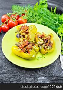 Pepper stuffed with mushrooms, tomatoes, zucchini, eggplant and onions, seasoned with wine, garlic, thyme and spices in a green plate, fork, parsley on wooden board background. Pepper stuffed with vegetables in green plate on wooden board