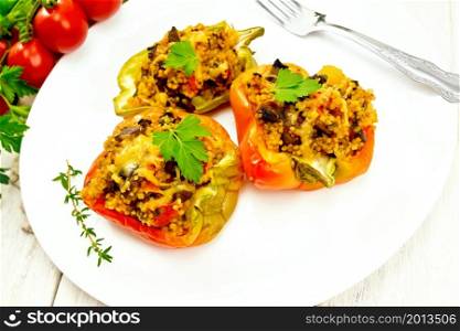 Pepper sweet, stuffed with mushrooms, tomatoes, couscous and cheese in a white plate on kitchen towel, fork, parsley against the background of wooden board