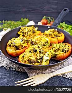 Pepper sweet, stuffed with mushrooms, tomatoes, couscous and cheese in an old frying pan on burlap, a fork, garlic, parsley and thyme against the background of black wooden board. Pepper stuffed with mushrooms and couscous in pan on burlap