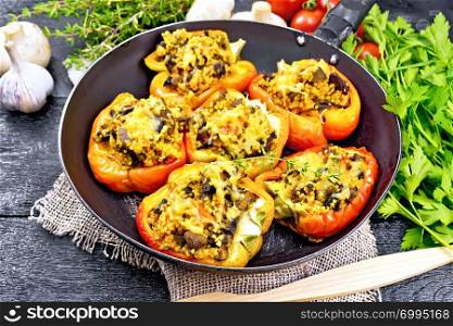 Pepper sweet, stuffed with mushrooms, tomatoes, couscous and cheese in an old frying pan on burlap, a fork, parsley and thyme against the background of dark wooden board