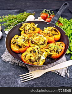 Pepper sweet, stuffed with mushrooms, tomatoes, couscous and cheese in an old frying pan on burlap, a fork, parsley and thyme against the background of wooden board