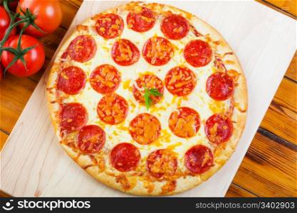 Pepperoni pizza on a wooden board with tomatoes.