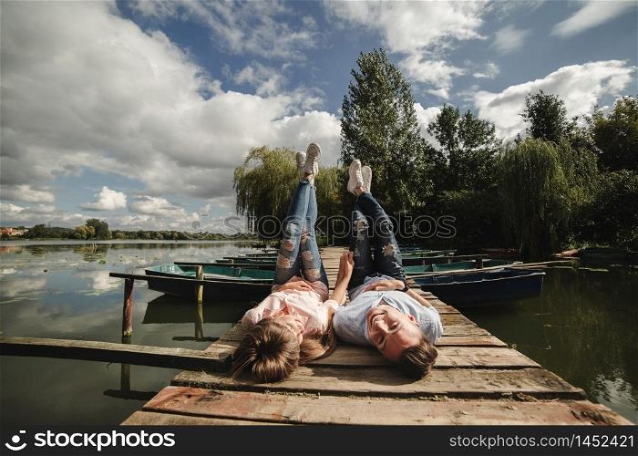 Perfect date. Beautiful young couple and smiling while lying on the pier. happy young man and woman laughing while lying on wooden pier near water