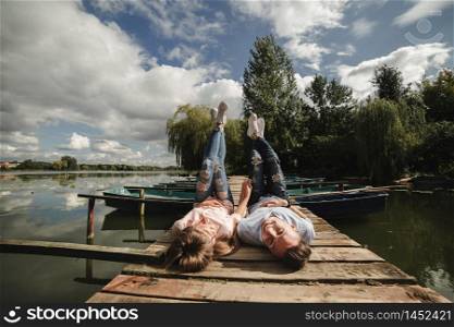 Perfect date. Beautiful young couple and smiling while lying on the pier. happy young man and woman laughing while lying on wooden pier near water