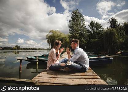 Perfect date. Beautiful young couple embracing and smiling while sitting on the pier. Ideal moment.. Ideal moment.. Beautiful young couple embracing and smiling while sitting on the pier