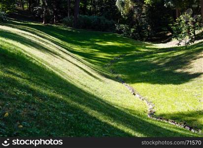 Perfect green grass lawn on landscape designed summer park hollow. Striped shadows on curved meadow surface of grass lawn.