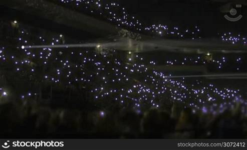Performance in the stadium at night. Crowd of people on stands waving with small flashlights