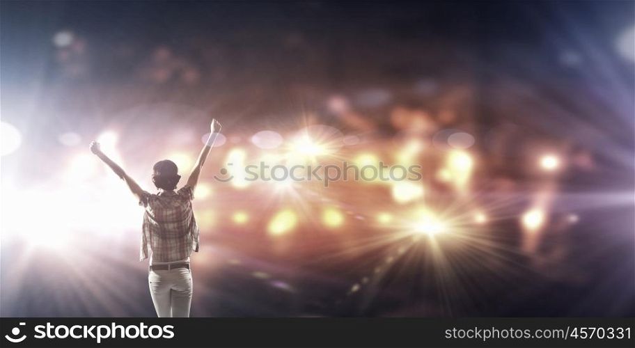 Performer on stage. Back view of girl with hands up standing in stage lights