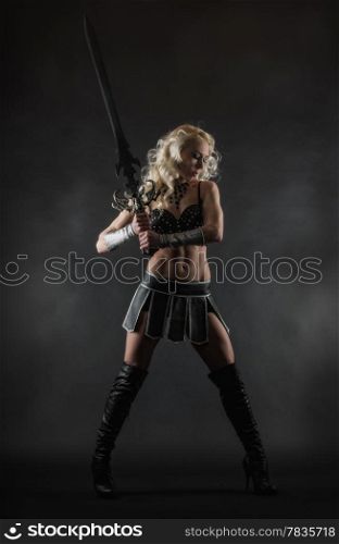Performer woman wearing sexy costume and holding a sword, grey smoky background
