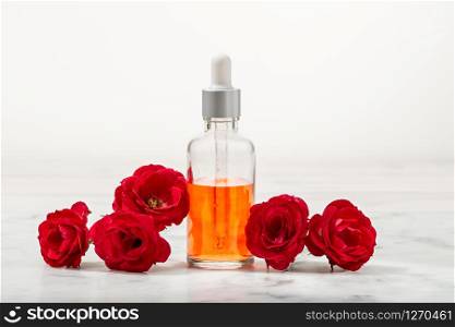 Perfumed Rose Water in glass bottle and small red roses with petals . Massage, aromatherapy and organic cosmetics concept