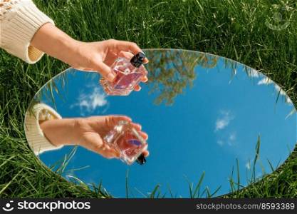 perfumery and nature concept - hand with bottle of perfume and sky reflection in round mirror on summer field. hand with perfume and sky reflection in mirror