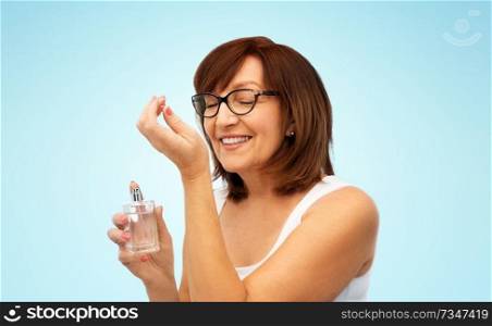 perfumery, beauty and luxury concept - happy smiling senior woman smelling perfume from her wrist over blue background. senior woman smelling perfume from her wrist