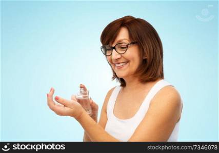 perfumery, beauty and luxury concept - happy smiling senior woman spraying perfume to her wrist over blue background. smiling senior woman spraying perfume to her wrist