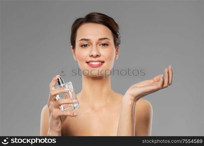 perfumery, beauty and luxury concept - happy smiling young woman with perfume over grey background. happy woman with perfume
